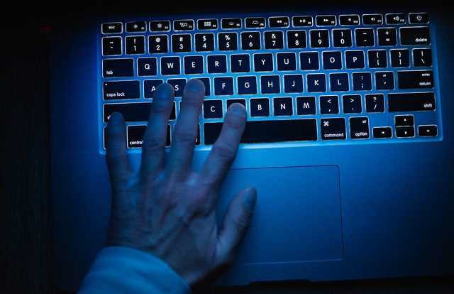 Bilde av hånd på et laptoptastatur med blått lys.